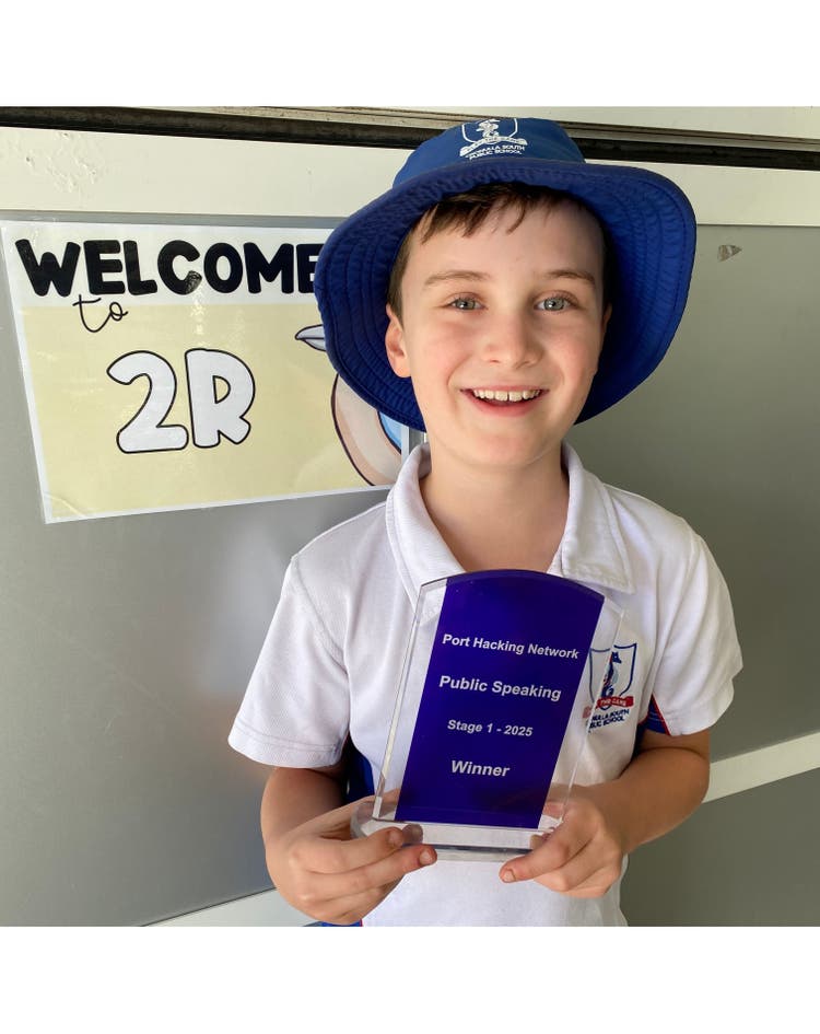 A boy smiling at the camera holding a public speaking award.