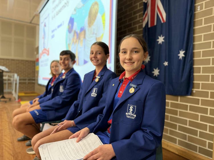 Four leadership students seated on a stage with a projector screen in the background.