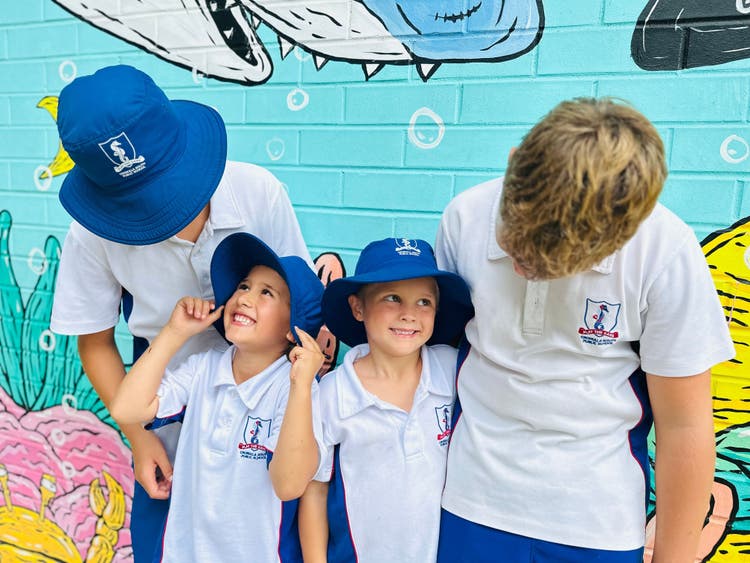 Two stage 3 students and two Kindergarten students standing in front of a mural.