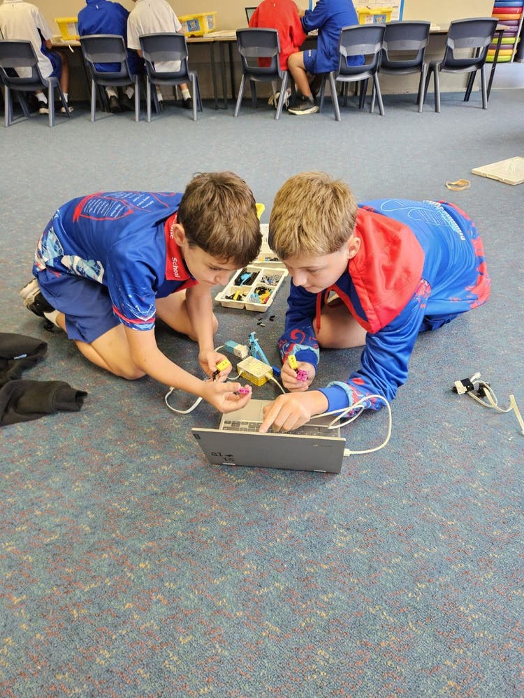 Two students working on a laptop with robotics attached.